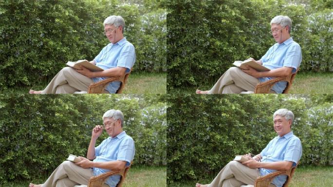 亚洲老人在家放松。亚洲高级中国男性享受休息时间戴眼镜看书，躺在花园里的早晨概念。
