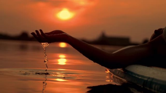 日落时在冲浪板上放松时，超级SLO MO女人用手舀水