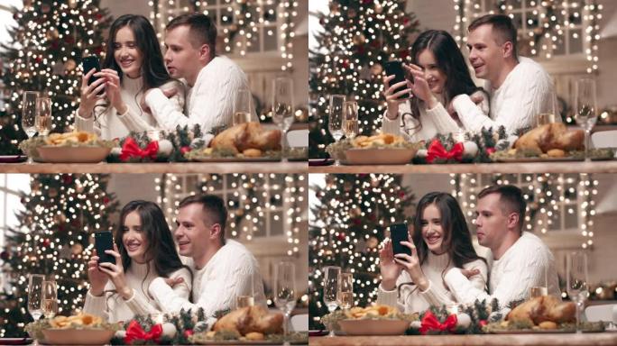 一对年轻夫妇在圣诞节餐桌上看着智能手机上的照片。在等待客人时，他们通过电话向父母和朋友发送圣诞节问候