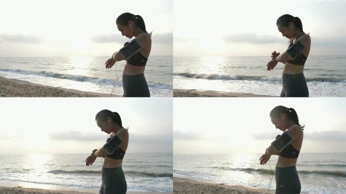 运动员亚洲女子在早上沙滩日出前跑步前设置和检查智能手表