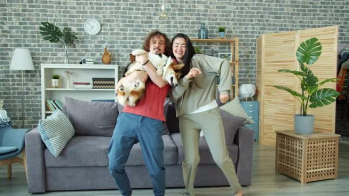 幸福的夫妇在家里跳舞，抱着威尔士柯基彭布罗克狗一起玩乐