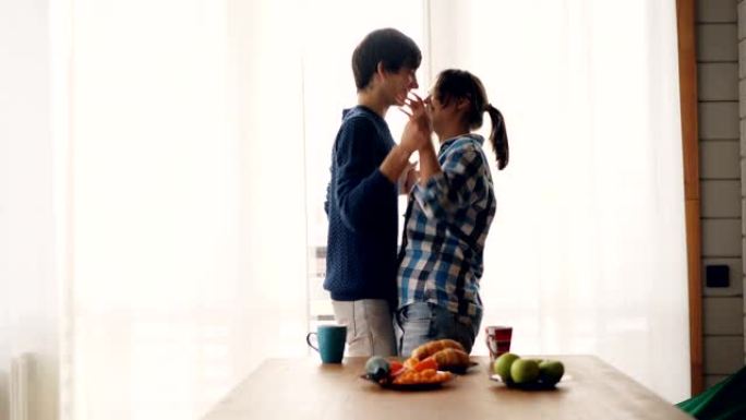 开朗的学生女孩和男孩在厨房里跳舞和接吻，在家听音乐，放松地表达爱和爱。青春和浪漫的概念。