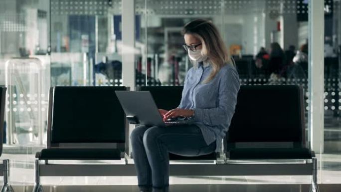 一位戴着安全面罩的女士正在大厅的笔记本电脑上打字
