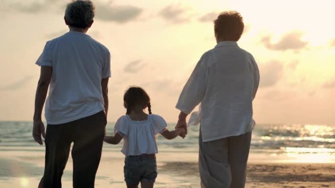 剪影快乐的祖父，祖母和孙女步行到沙滩上日落冲浪。家庭，生活方式，人，孩子，人寿保险，老人，假期，关系