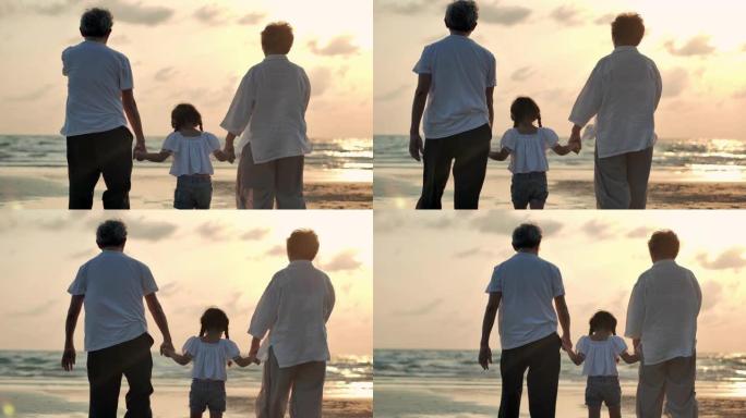 剪影快乐的祖父，祖母和孙女步行到沙滩上日落冲浪。家庭，生活方式，人，孩子，人寿保险，老人，假期，关系