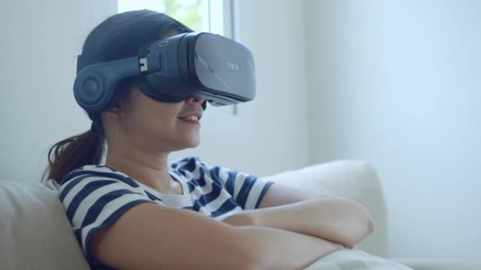 时髦的亚洲女性在家里使用虚拟现实模拟器眼镜。