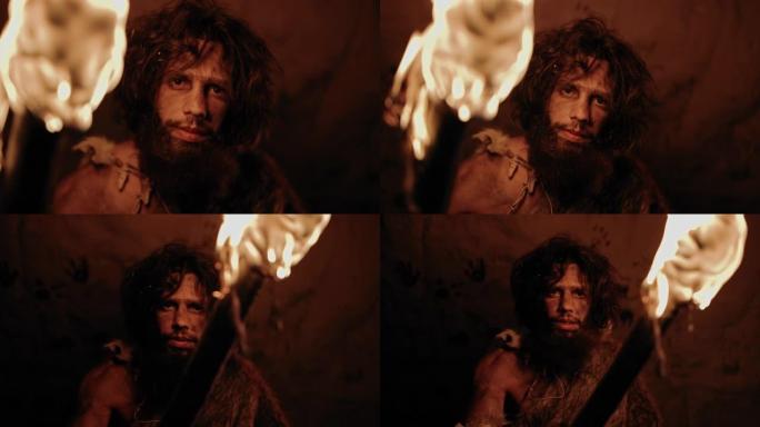 原始穴居人的肖像在晚上站在他的洞穴中，戴着兽皮，拿着火把。原始尼安德特人猎人/智人晚上独自在他的巢穴