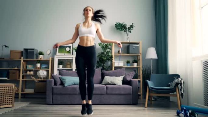 苗条的年轻女运动员在公寓里跳绳，专注于有氧运动