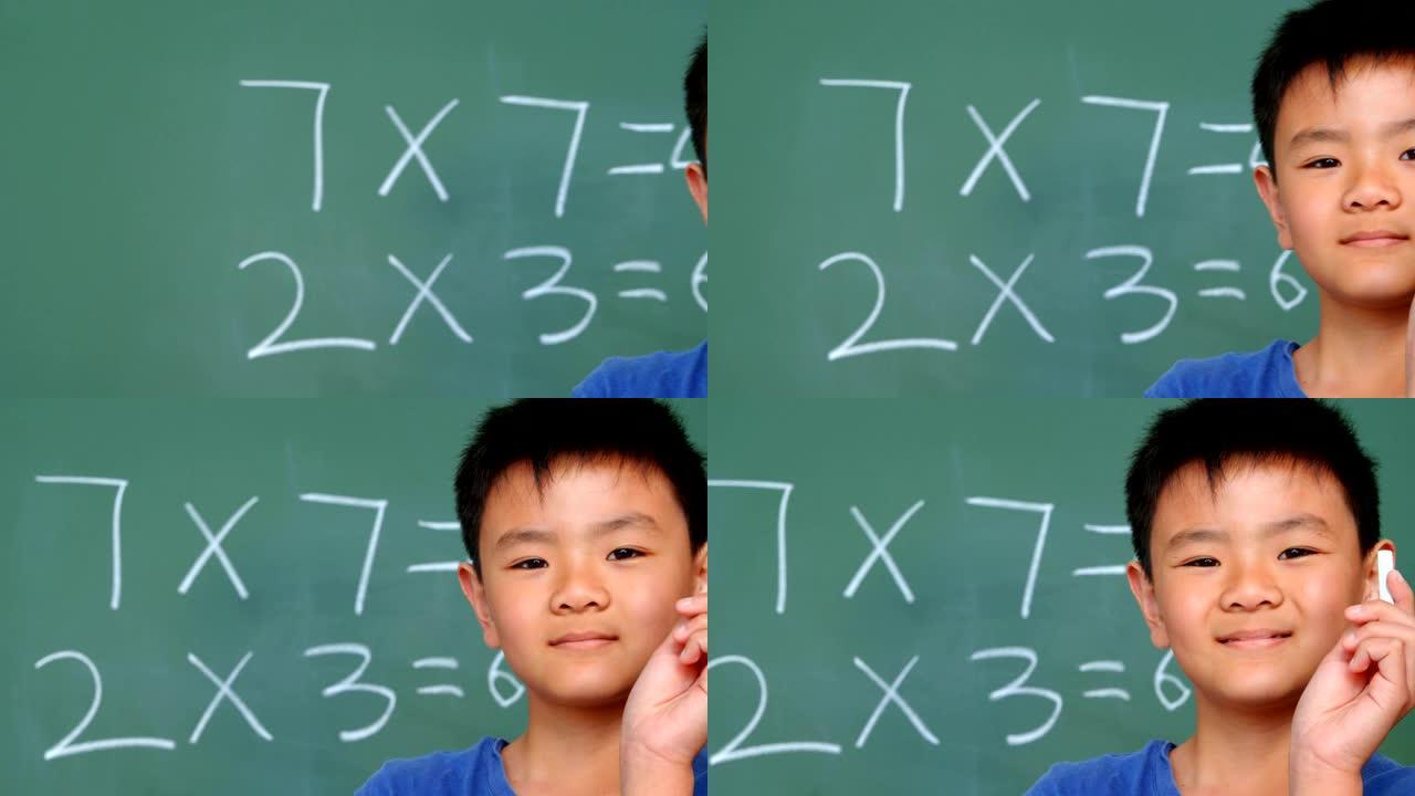 亚洲男生站在黑板上并在教室里展示粉笔的前视图4k