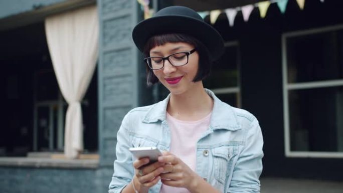 快乐的年轻女子在城市街道触摸屏户外使用现代智能手机