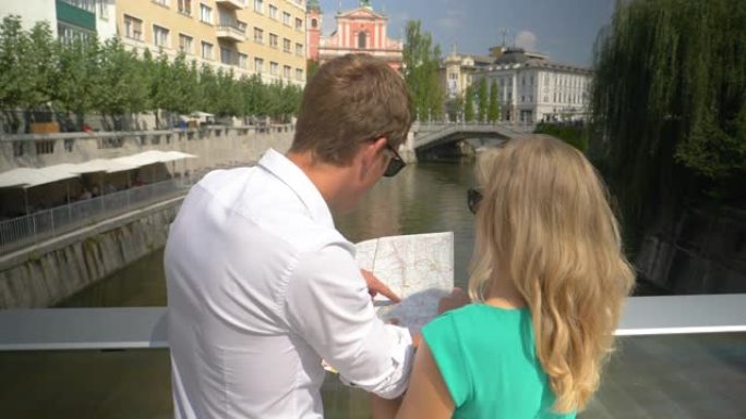 慢动作夫妇看着地图，指着阳光明媚的卢布尔雅那的建筑物