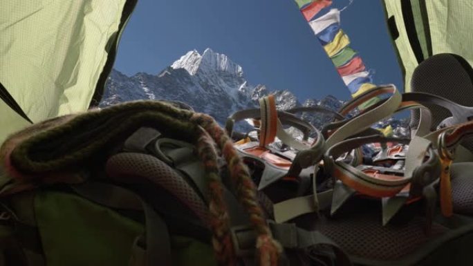在尼泊尔喜马拉雅山旅行。准备爬山。相机在帐篷内移动，那里有睡袋，背包，冰爪，靴子。佛教旗帜随风飘扬。