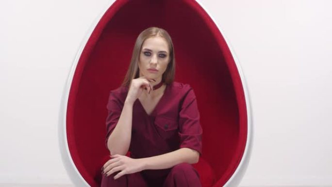 优雅的时尚模特在工作室的红蛋椅上摆姿势