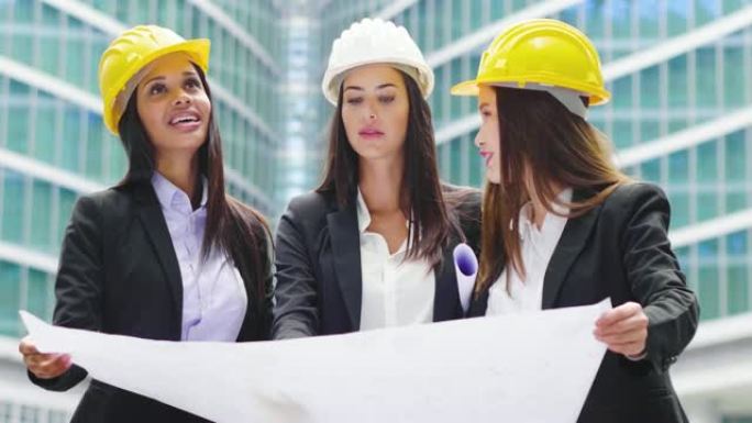 三名不同种族 (亚洲，欧洲和美国黑人) 戴着头盔的工程师妇女观看了一个建筑项目，并讨论了如何继续工作
