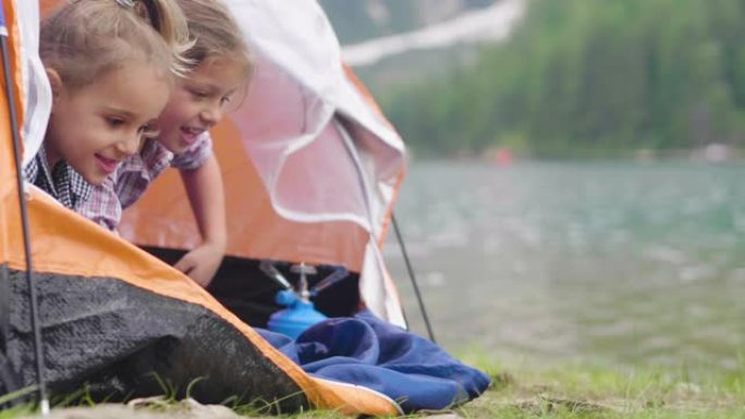 两个姐妹在湖边露营，他们喜欢在帐篷里玩耍，周围是大自然。
