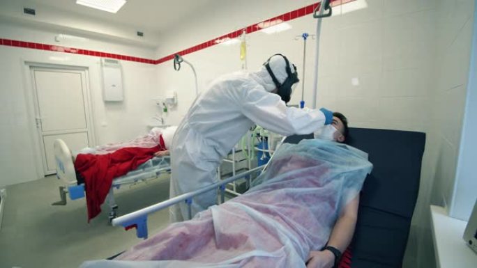 穿着防护服的医生正在检查说谎的病人的体温。新型冠状病毒肺炎，大流行，病毒，冠状病毒疾病，世界流行，冠