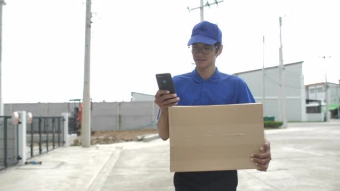 送货员拿着包装箱在房屋村的智能手机上寻找客户