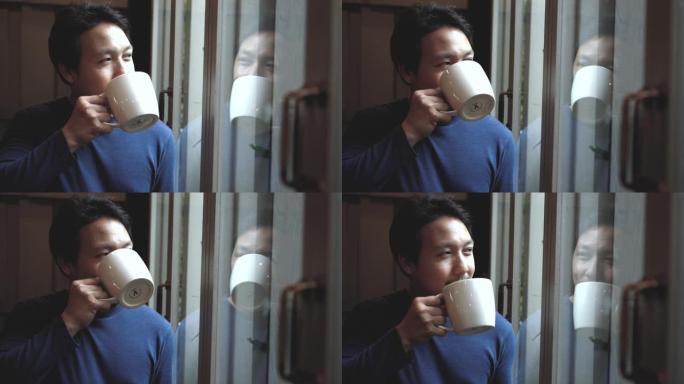 4k慢动作镜头亚洲帅哥站在窗玻璃旁喝着咖啡，带着活泼的微笑，从咖啡馆向外看，生活方式和休闲理念
