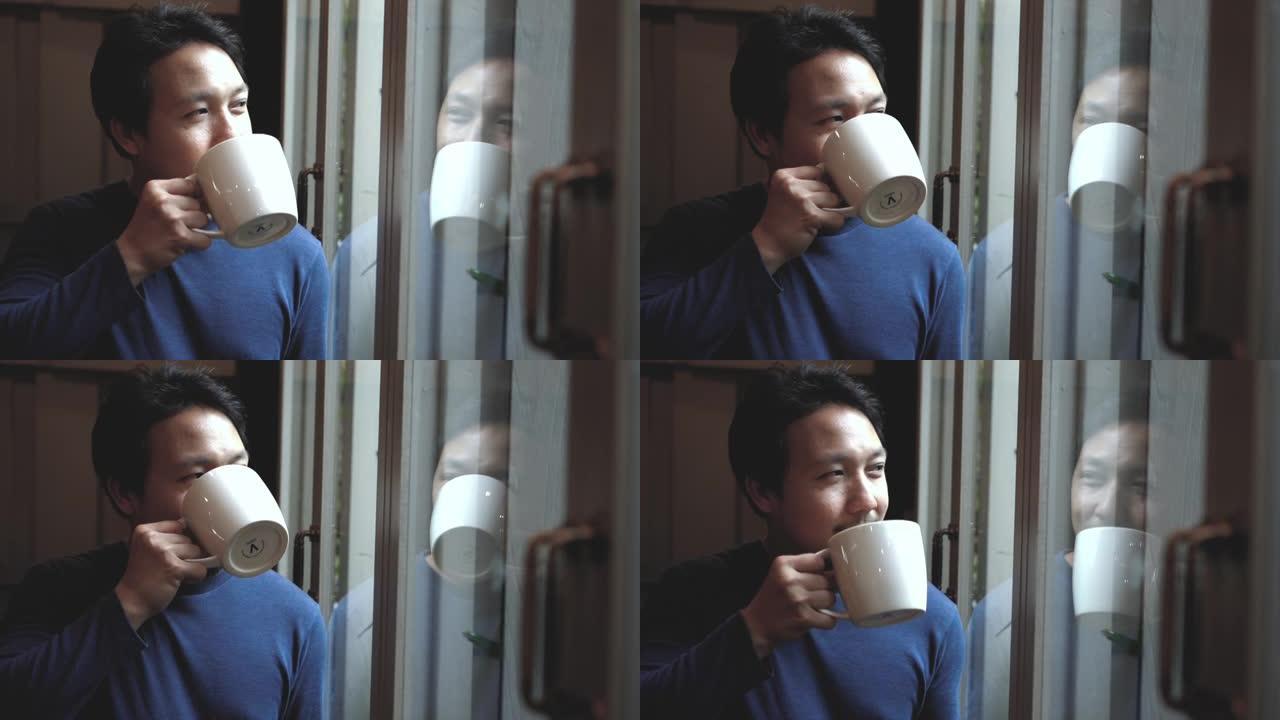 4k慢动作镜头亚洲帅哥站在窗玻璃旁喝着咖啡，带着活泼的微笑，从咖啡馆向外看，生活方式和休闲理念