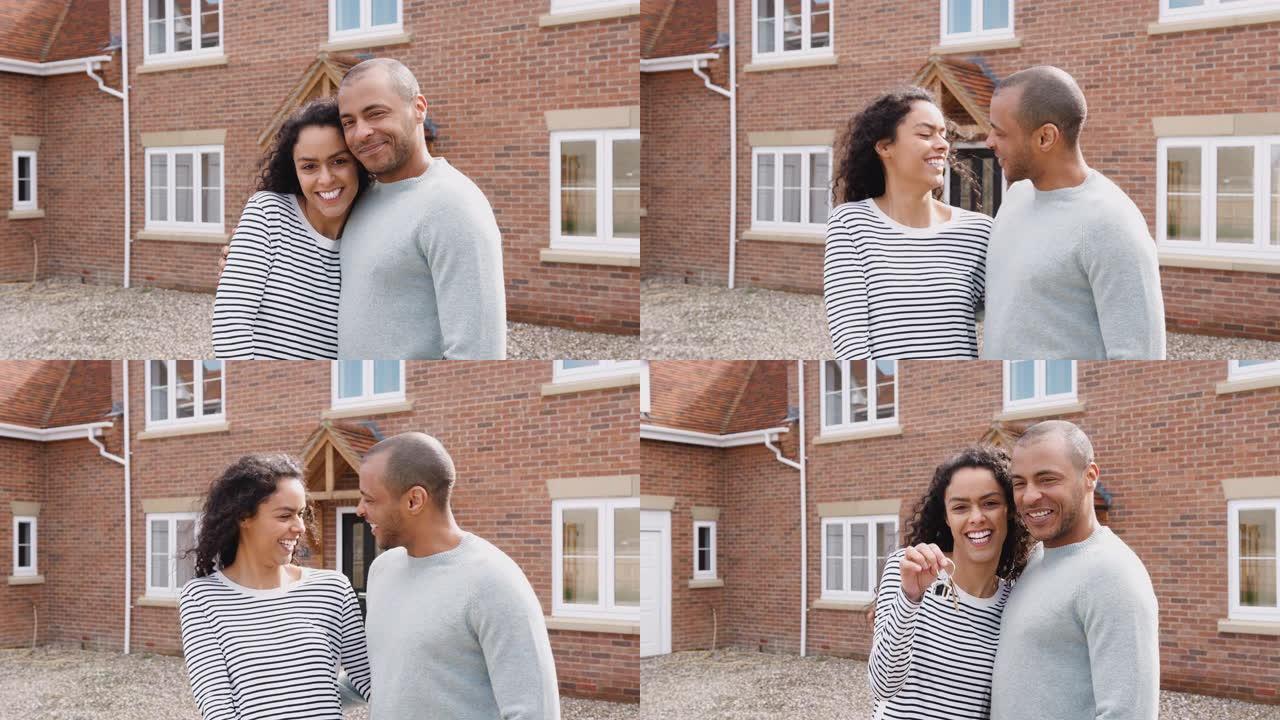 激动的夫妇站在新家外面拿着钥匙，微笑着慢动作镜头的肖像