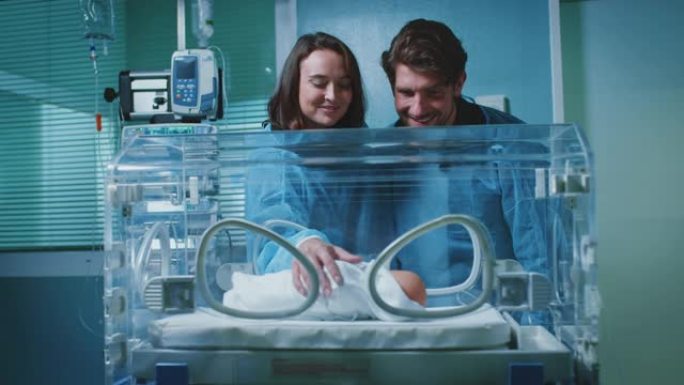 微笑的年轻夫妇在孵化器中抚摸婴儿