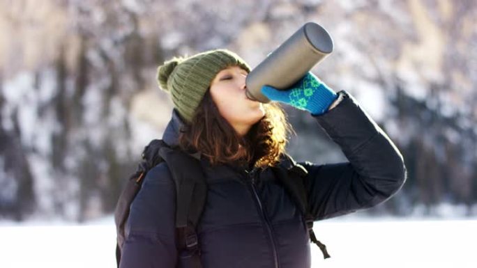 女孩从水瓶中喝淡水来解渴，并为背景降温雪山和松林。山的纯净水。