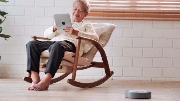亚洲老年女性患者使用平板电脑与医生进行视频会议，而机器人真空吸尘器则完成所有工作。高级假期，技术，人