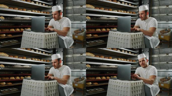英俊的年轻面包师学生的慢动作使用笔记本电脑进行在线学习，并在面包店学习课程，背景是面包和烤箱。
