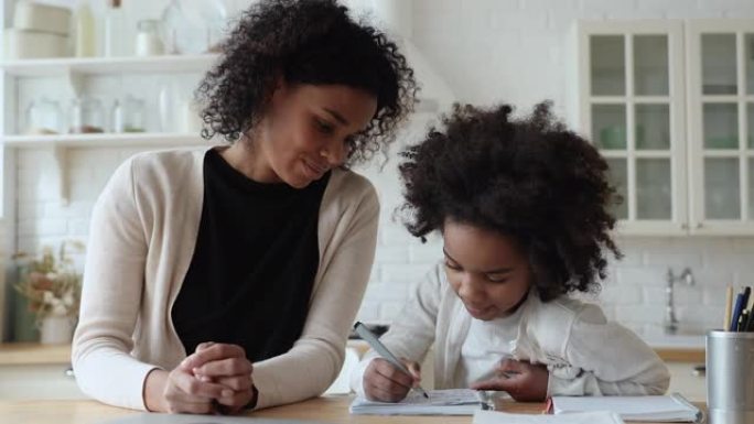 美国黑人妈妈帮助可爱的小学生女儿检查作业
