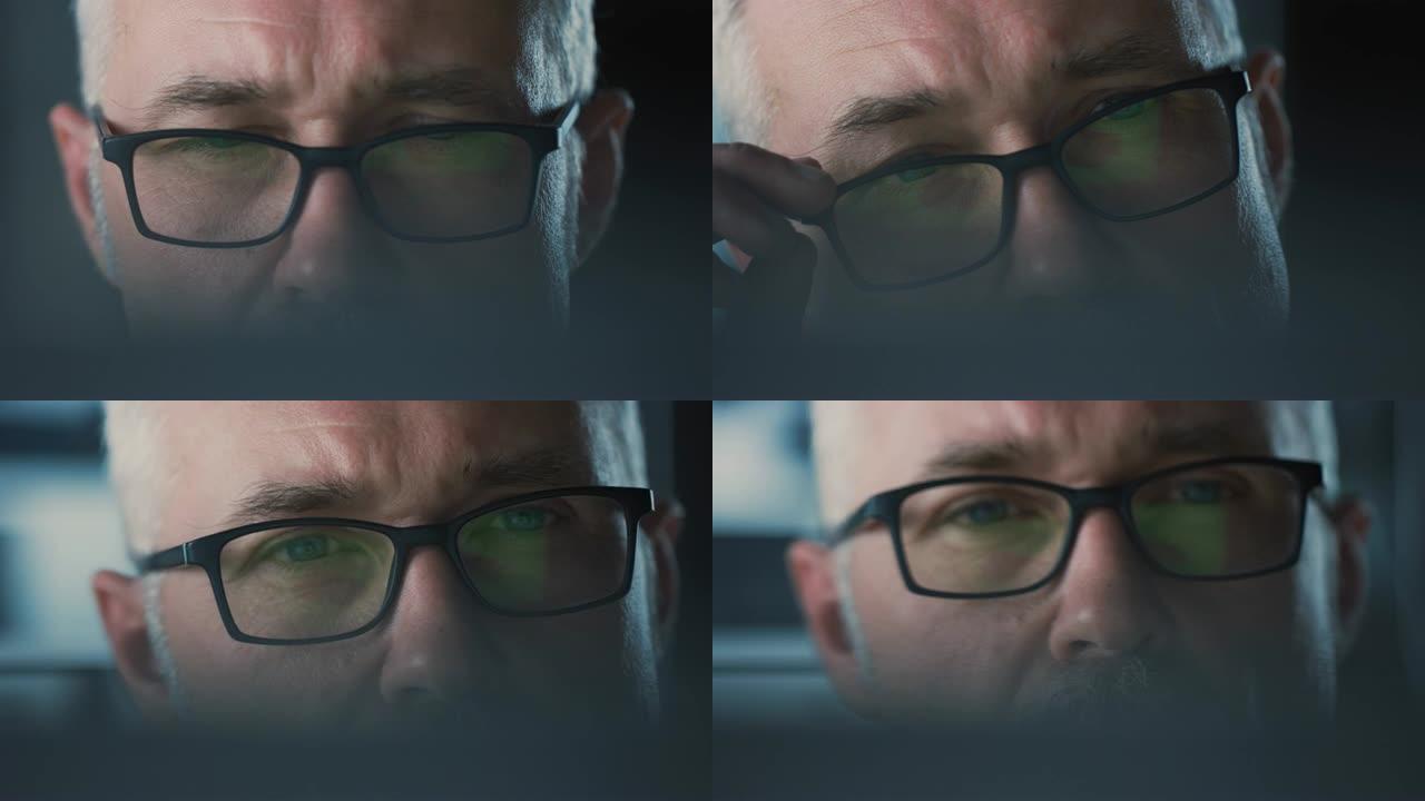 戴着眼镜在电脑上工作的英俊中年男子的特写肖像。迷人的白发蓝眼睛男人