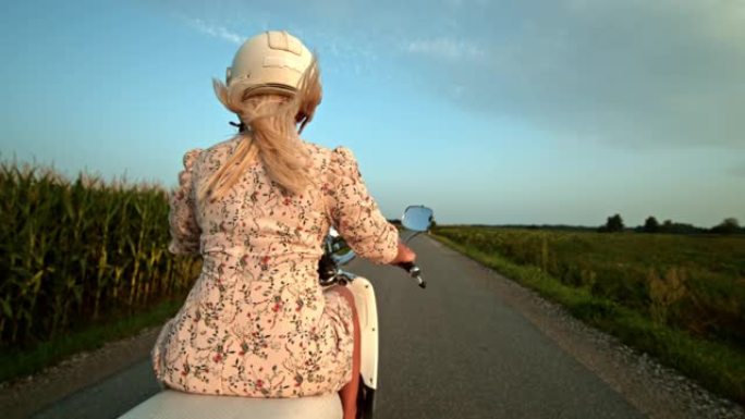 超级SLO MO女人在乡村道路上骑踏板车