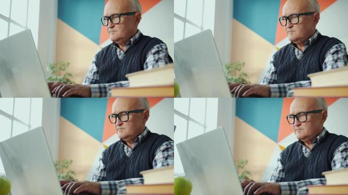 退休男子在公寓的办公桌上使用笔记本电脑打字的慢动作