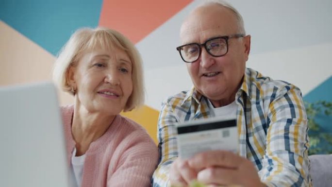 老年男女在家使用笔记本电脑在线购物用银行卡付款