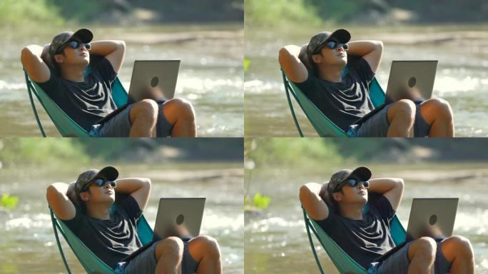 用笔记本电脑在河里的野餐椅上放松的人。
