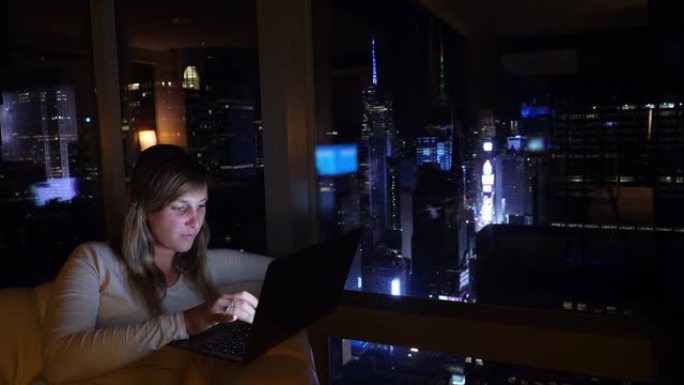 特写: 出差的女人坐在酒店房间里，晚上可以看到纽约的景色。