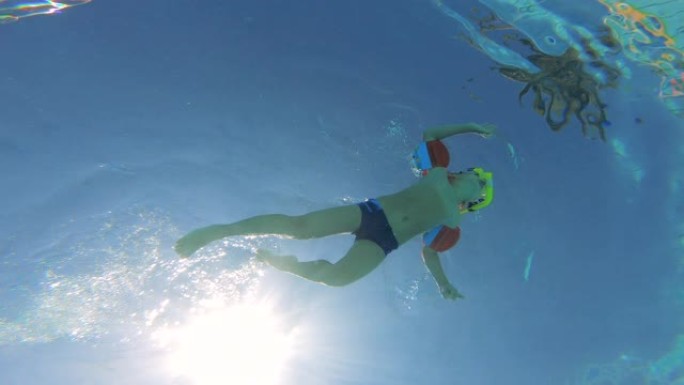 一个男孩戴着臂章在游泳池里游泳的水下镜头。