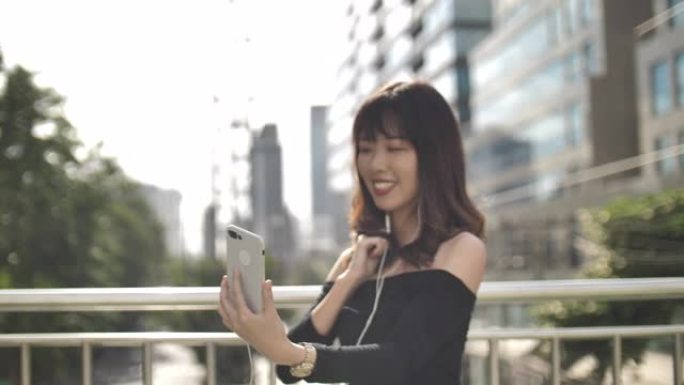 一个美丽的年轻女子的肖像在街上用电话听音乐，跳舞，快乐的微笑