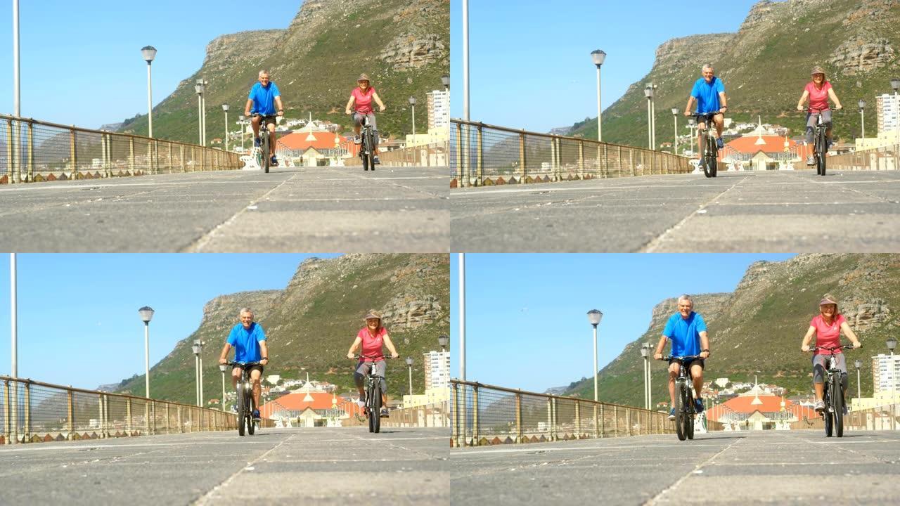 活跃的高级高加索夫妇在海滩4k的长廊上骑自行车的前视图