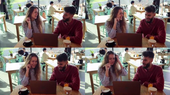 年轻的金发女人和中东男人在咖啡馆使用笔记本电脑