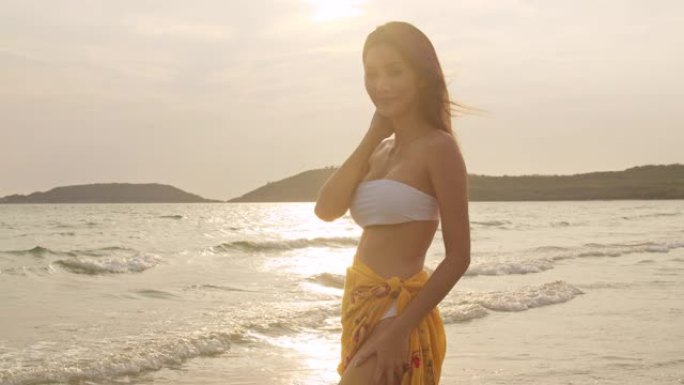 亚洲女人在沙滩上微笑。穿着比基尼的年轻快乐女性在日落时在热带海洋附近放松和有趣的微笑，同时度假、暑期