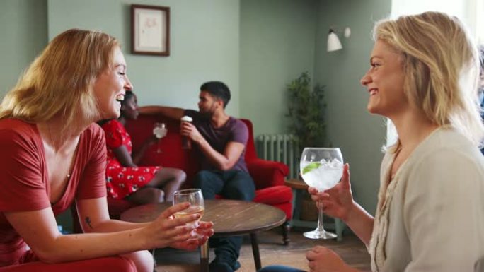 两名年轻的成年白人妇女坐在一起大笑，在酒吧的休息室里聊天和喝酒，特写镜头