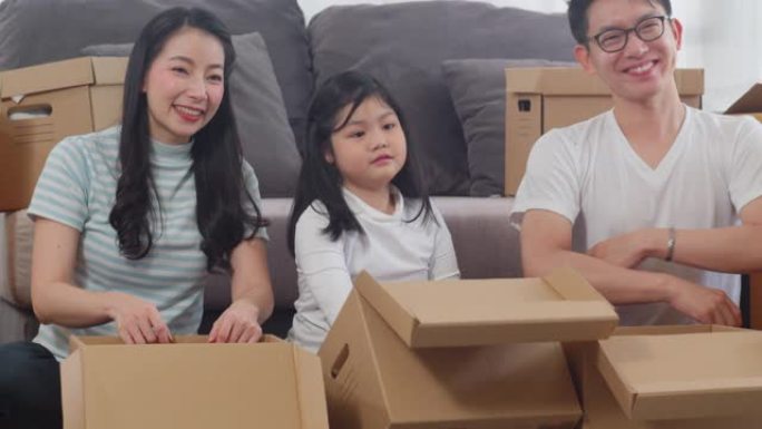 快乐的亚洲年轻家庭搬迁搬迁定居新家。搬家当天，中国父母和孩子在客厅打开纸箱或包裹拆箱。房地产住宅、贷