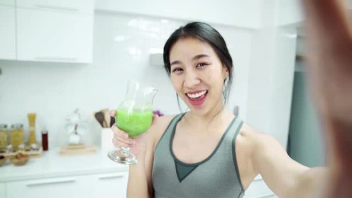 POV: 年轻的亚洲女性在周末早上在厨房里使用智能手机，自拍和喝苹果的smooties。健康饮食和健