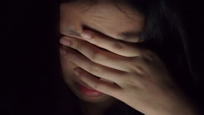 特写镜头的女人在黑暗的房间里使用智能手机会感到疲倦，眼睛疼痛和头痛