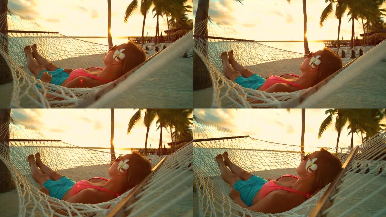慢动作: 放松的女人躺在吊床上在沙滩上摇摆。