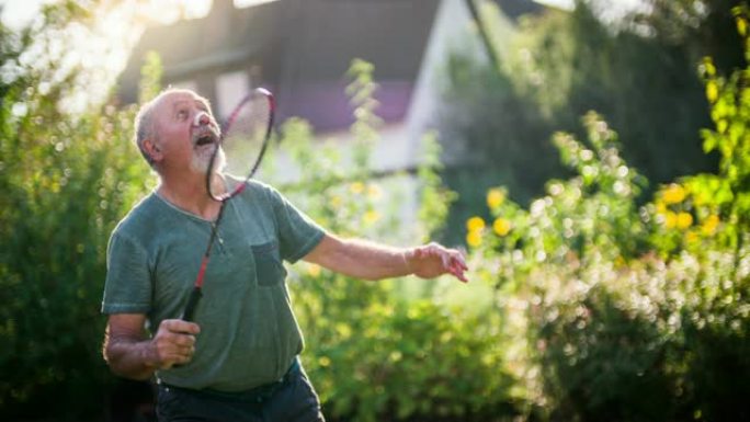 活跃的老年人在阳光普照的花园里打羽毛球