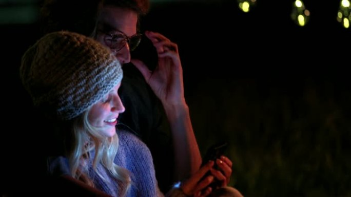 夫妇在夜间露营时看着手机