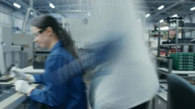 男人和一个穿着蓝色和白色工作外套的年轻女性正在使用镊子为智能手机组装印刷电路板。高科技工厂设施中的电