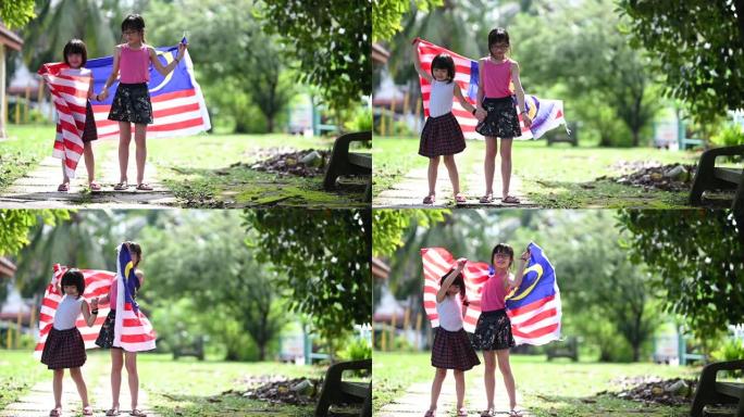 两个亚洲中国小女孩在公园玩，花时间与马来西亚国旗包装