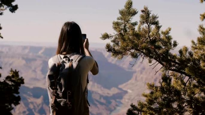后视图快乐的年轻旅游女人在美国亚利桑那州拍摄史诗大峡谷山风景的智能手机照片。